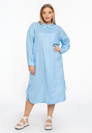 Helles blaues Hemdblusenkleid mit langen Ärmeln, seitlichen Bindegürteln und einem geschwungenen Saum, gefertigt aus einem glatten Stoff mit einem subtilen Glanz.