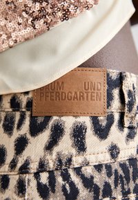 Beige and black leopard print denim shorts with a brown leather label reading "BAUM UND PFERDGARTEN." Textured sequined top above.