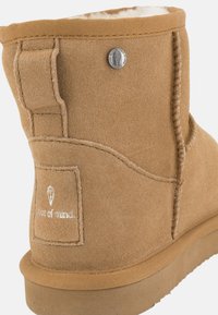 Stivale alla caviglia in suede tan con punta rotonda, cuciture laterali e una patch con logo. Presenta un morbido rivestimento interno e una suola in gomma testurizzata.