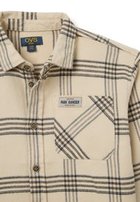 Beige flanellen overhemd met zwart en marineblauw ruitpatroon, knopen aan de voorkant, een borstzak en een "Park Ranger" label.