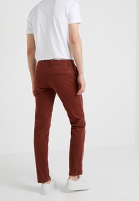 Bruna slim-fit byxor med en slät textur, med bakfickor och en logotagg. I kombination med en enkel vit t-shirt och vita sneakers.