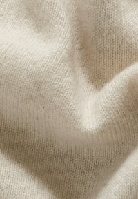 Weiches, gestricktes Material in einem hellen Cremeton, das eine feine Textur mit dezenten Rippungen und einem leicht flauschigen Aussehen zeigt.