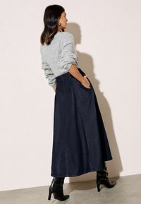 Szürke pulóver, felg rolled ujjal, párosítva egy hosszú, sötétkék farmer szoknyával, amely oldalsó zsebekkel rendelkezik. Fekete magassarkú csizmák egészítik ki a megjelenést.