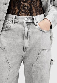 Jeans de mezclilla gris con un lavado desgastado, con bolsillos frontales, cierre de botones y costuras detalladas. Combinados con una blusa con superposición de encaje.