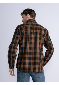 Camisa de cuadros negra y naranja con mangas largas, puños abotonados y un cuello clásico, hecha de tejido tejido. Presenta un dobladillo curvado.