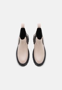 Bottines en cuir beige avec accents noirs, bout rond, semelle épaisse et languette arrière pour un enfilage facile, avec des panneaux latéraux en élasthanne.