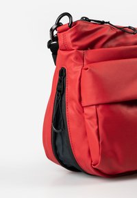 Red nylon bag with a zippered pocket, rounded shape, black hardware, and textured surface. Features adjustable strap and top closure.