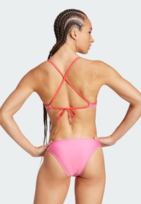 Bikini rosa con spalline incrociate, dettaglio con nodo sul retro e parte bassa a vita bassa. Tessuto liscio e elastico con un colore uniforme.