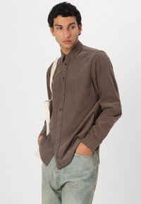 Braunes, langärmliges Hemd mit Knöpfen aus einem weichen Material, mit Kragen, Vorderknöpfen und einem entspannten Schnitt, kombiniert mit hellen Jeans.
