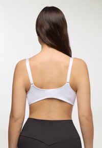 Reggiseno bianco in tessuto morbido con spalline regolabili e chiusura con gancetto sul retro. Abbinato a leggings neri a vita alta.