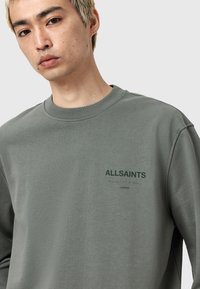 Grön crewneck sweatshirt med ribbad krage, med "ALLSAINTS LONDON"-logotyp i mörkgrön, mjuk tygkvalitet och standardpassform.