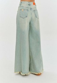 Světlé modré volné džíny s třepeným lemem, vysokým pasem a dvěma zadními kapsami. Na pásku se nachází obdélníková béžová etiketa.