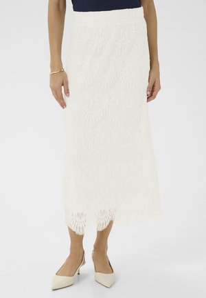 Jupe midi en dentelle blanche avec un ourlet festonné et un motif floral, dotée d'une taille cintrée et d'un tissu texturé. Associée à des talons de couleur claire.