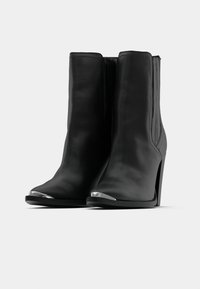 Melnas ādas potītes zābaki ar augstu papēdi, atvērtu purngalu un metāla purngalu. Satur vertikāls šuvums un gludu tekstūru.