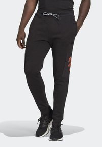 Černé slim-fit tepláky s elastickým pasem, které mají modrou a bílou šňůrku a oranžovou nášivku loga Adidas na bocích.