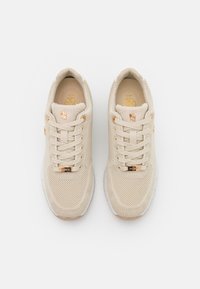 Beige sportovní boty vyrobené z mřížkového materiálu s texturovaným povrchem, s zlatými akcenty a bílou gumovou podešví.