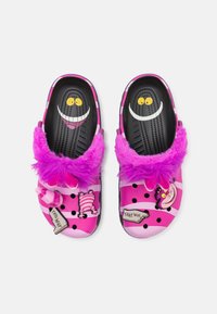 Roze instapklompen met zwarte stippen, fuzzy paarse rand en cartoonfiguren; met gele ogen en glimlachdetails.