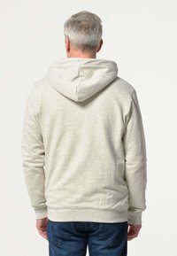 Lichtgrijze hoodie met een zachte textuur, met een centrale naad op de rug en geribbelde manchetten. Gecombineerd met blauwe spijkerbroek.