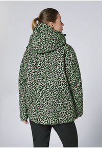 Grüne Leopardenmuster-Jacke mit rosa Akzenten, mit Kapuze, lockerem Schnitt und schwarzen Details, aus der Rückansicht gezeigt.