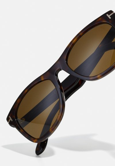 Ochelari de soare tortoiseshell maro cu lentile graduat maro, având un cadru gros și un logo T proeminent pe laterale.