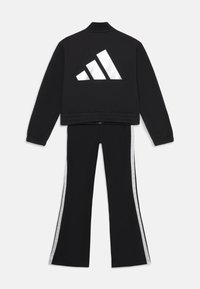 Chándal deportivo negro que incluye una chaqueta corta con un logo trefoil blanco reflectante y pantalones a juego con rayas plateadas en los lados.