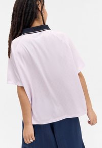 Ανοιχτό μωβ κοντομάνικο πουκάμισο με μαύρο κολάρο, με διακριτά σχέδια, χαλαρή εφαρμογή και λεία υφή. Εμφάνιση από πίσω.