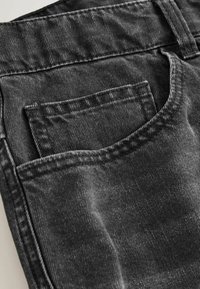 Gros plan sur la poche d'un jean en denim noir avec les coutures visibles et la texture du tissu.