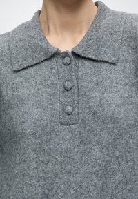 Gros plan d'un pull gris en maille avec un large col et trois boutons recouverts de tissu sur le devant.
