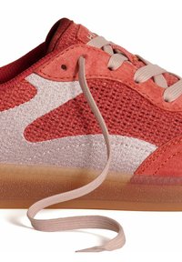Sneaker rouge avec un dessus en mesh et en daim, des accents rose pâle, une pointe ronde, et une semelle en caoutchouc transparente avec un design texturé.