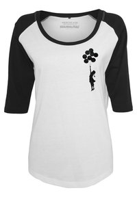 Witte shirt met zwarte raglanmouwen. Bevat een zwarte silhouet van een kind dat ballonnen vasthoudt, met een gladde textuur en een casual ontwerp.