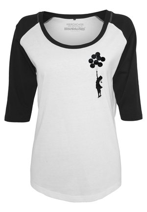 Camisa blanca con mangas raglán negras. Presenta una silueta negra de un niño sosteniendo globos, exhibiendo una textura suave y un diseño casual.