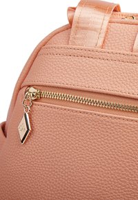 Zaino sintetico rosa, caratterizzato da una superficie strutturata, hardware della cerniera dorato e un piccolo tag decorativo sulla tasca frontale.