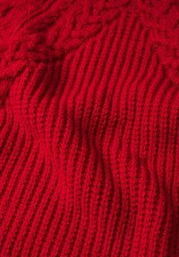 Maglione rosso lavorato a maglia con un motivo a coste texturizzato e trecce, che mostra un aspetto morbido e caldo.