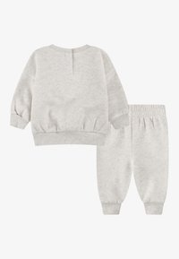 Sweatshirt gris clair et pantalon de jogging assorti, tous deux en matériau doux. Comprend des poignets et une taille côtelés, avec un détail de bouton au dos du haut.