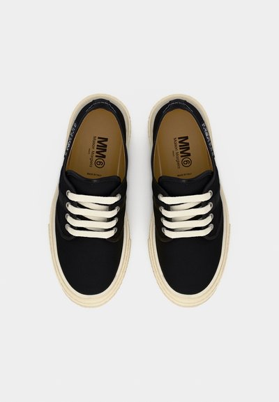 Ζευγάρι μαύρα πάνινα παπούτσια χαμηλού παπουτσιού με λευκά κορδόνια και μπεζ λαστιχένιες σόλες, που εμφανίζουν το λογότυπο MM6 Maison Margiela στο εσωτερικό.