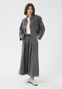 Grå denimjacka med knappar, två bröstfickor; matchande grå vida byxor, avsmalnande i botten; modellen bär ljusa skor.