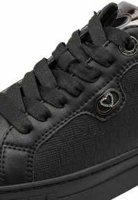 Black sneaker featuring textured synthetic upper, woven laces, metal accent with a heart design, and a sturdy rubber sole.