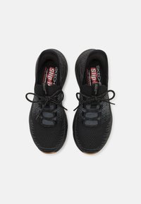 Zapatillas deportivas negras con parte superior de punto, superficie texturizada, puntera reforzada y cordones tradicionales. Suela de goma, acentos de logo en el talón y en la lengüeta.