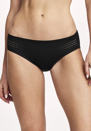 Frau trägt schwarze Hipster-Unterwäsche mit kleinen perforierten Designdetails an den Seiten, gezeigt vom mittleren Rumpf bis zu den oberen Oberschenkeln.