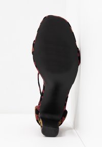 Sandale avec semelle noire et talon bloc, avec des brides en tissu coloré aux motifs rouges, jaunes et noirs.