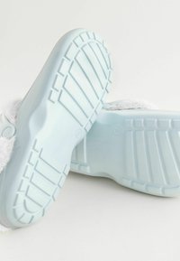 Hellblaue Gummisohlen mit einem strukturierten Gripmuster; begleitet von weichen grauen Fellakzenten im oberen Bereich.