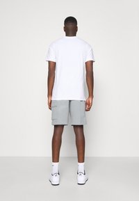 Vit t-shirt med kort ärm matchad med ljusgrå cargoshorts. Modellen bär vita sneakers och vadlånga strumpor. En enkel bakgrund.