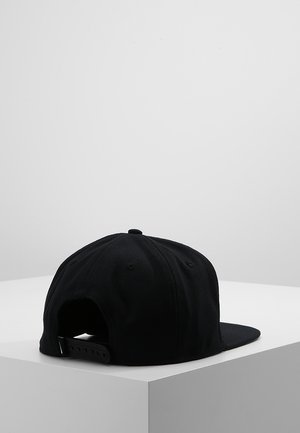 Czarna czapka snapback z płaskim daszkiem umieszczona na białej powierzchni narożnej, pokazana od tyłu z widocznym regulowanym paskiem.