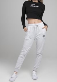 Black long-sleeve crop top with white script logo; gray joggers with side pockets and embroidered logo. White sneakers complete the outfit.