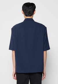 Camisa de manga corta en azul marino oscuro con rayas verticales, confeccionada en tela ligera, con cuello clásico y espalda de corte recto.