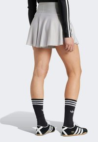 Falda corta gris con un diseño acampanado, tejido texturizado y una cinturilla suave. Combinada con calcetas negras a rayas y calzado negro.