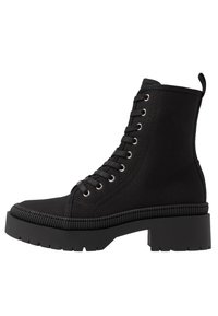 Bottine noire à tige en toile, design à lacets, bout arrondi, œillets argentés et semelle en caoutchouc épaisse avec bord texturé.