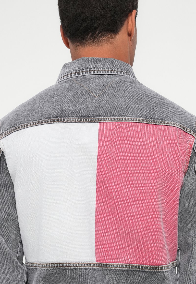 Denimjacke mit einem grauen Abschnitt auf der Rückseite, einem weißen Quadrat und einem roten Quadrat. Sichtbare Nähte und ein klassisches Kragen-Design.