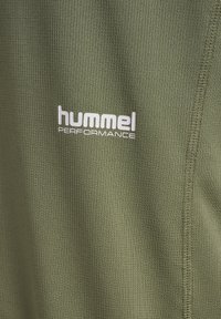 Grønt tekstureret stof med hvidt "hummel PERFORMANCE" logo og lodrette sømme på højre side.