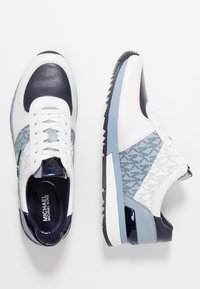 Baskets blanches et bleu marine avec des panneaux en cuir et tissu, design bleu texturé, bout arrondi, et une semelle extérieure en caoutchouc à rainures.